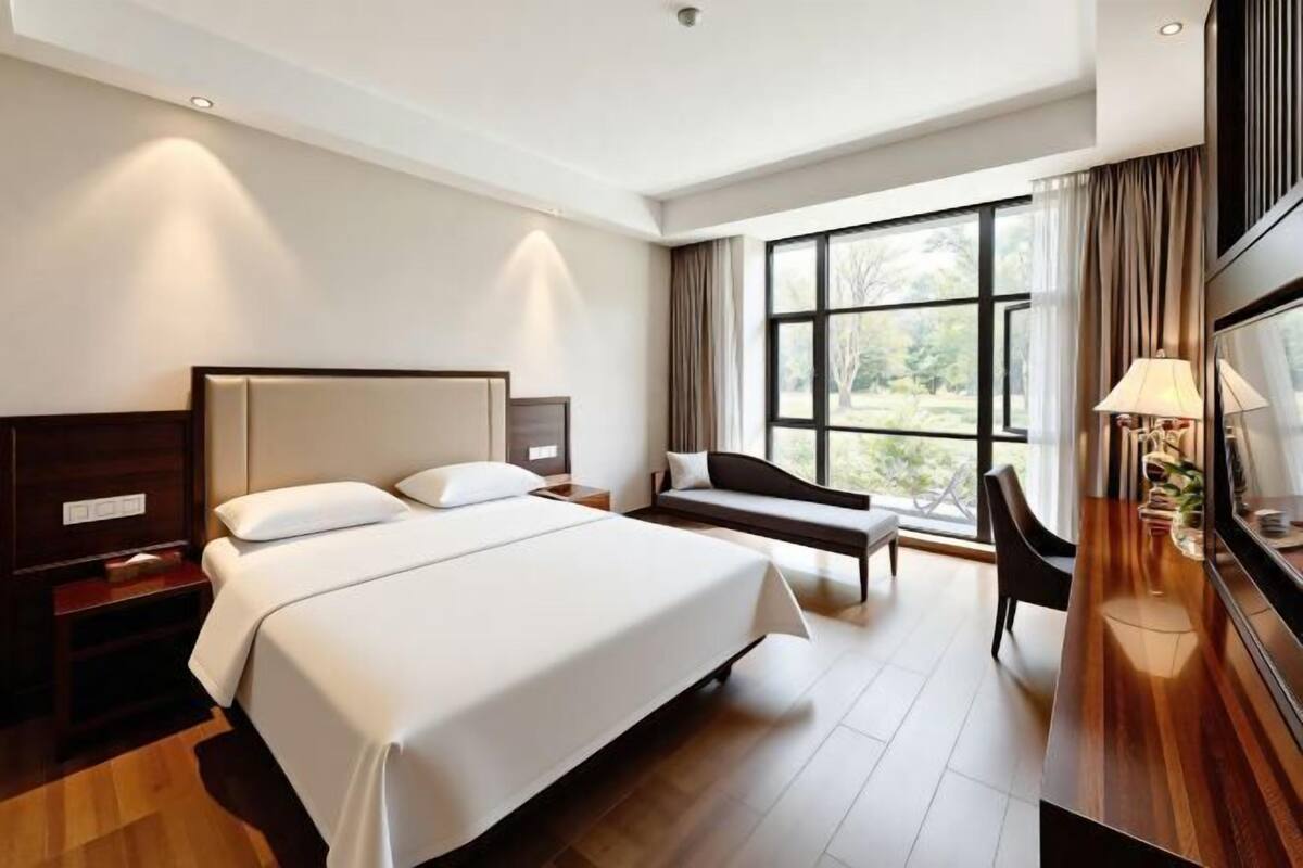 Ein Hotelzimmer mit Bett, Nachttischen, Schreibtisch, Stuhl und einem großen Fenster.