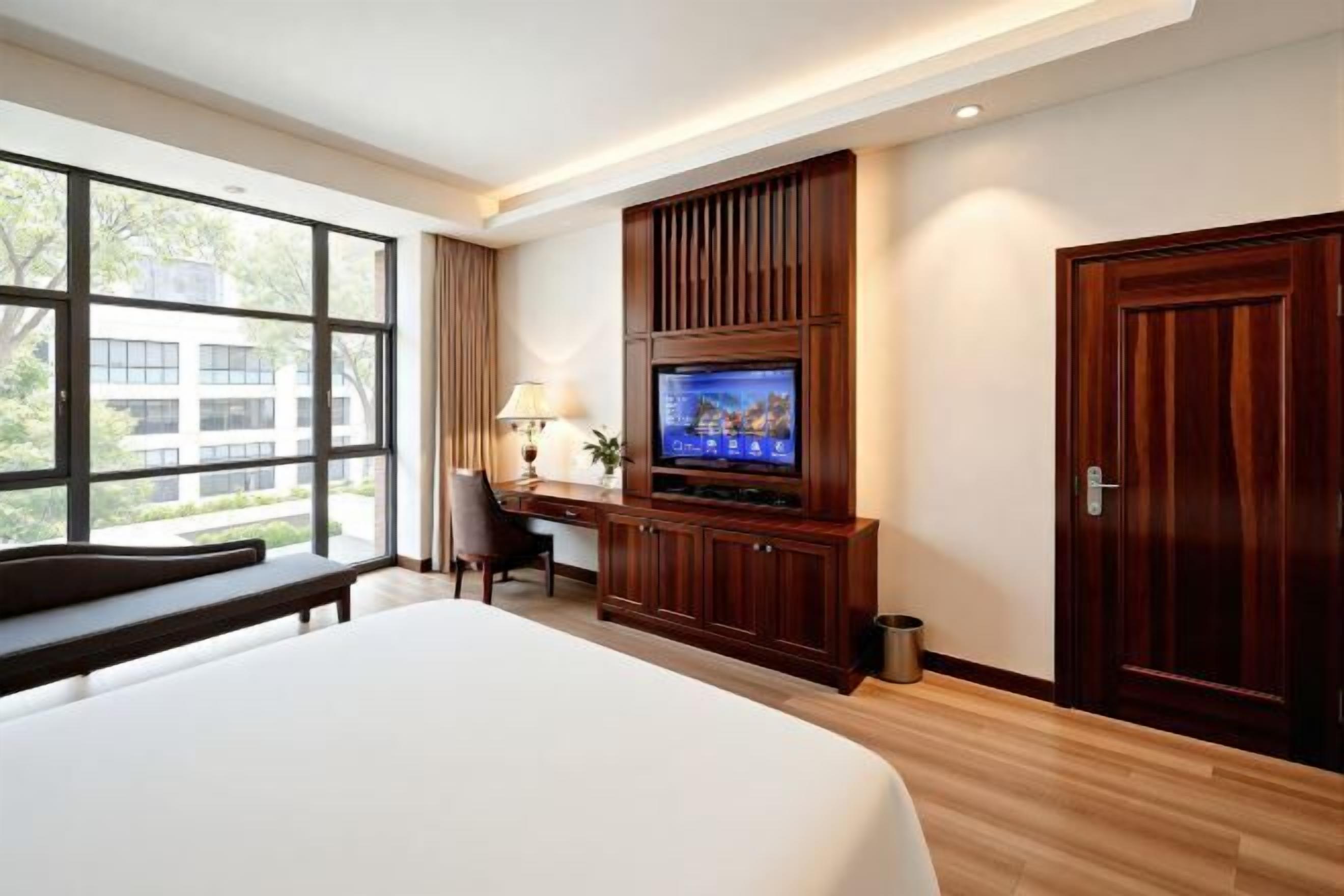 Ein Hotelzimmer mit einem großen Bett, einem Schreibtisch mit Fernseher, einem Fenster mit Aussicht und einer Tür.
