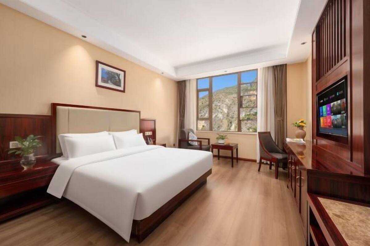 Ein Hotelzimmer mit einem großen Bett, einem Schreibtisch mit Stuhl, einem Fernseher und einem Fenster mit Blick ins Freie.