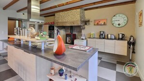 A modern kitchen with a central island, stone wall, and a clock on the wall. - La Petite Prairie - Baguer Morvan (BAGUER MORVAN)