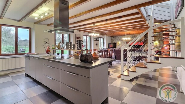 A modern kitchen with a central island, a staircase, and a dining area. - La Petite Prairie - Baguer Morvan (BAGUER MORVAN)