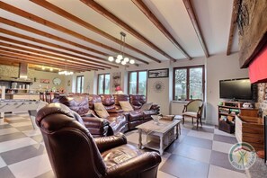 Un salón amplio con un sofá de cuero, una mesa de centro y un televisor. Se observa una cocina al fondo con una zona de comedor.