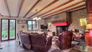 A living room with leather sofas, a stone fireplace, a television, and a large window overlooking a garden. - La Petite Prairie - Baguer Morvan (BAGUER MORVAN)