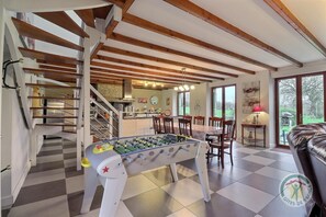 Amplia sala de estar con mesa de fútbol, comedor y escalera que sube a un piso superior.