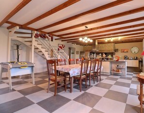 A dining area with a checkered floor, wooden chairs, a table with a tablecloth, a foosball table, a kitchen area with a stove, and a staircase. - La Petite Prairie - Baguer Morvan (BAGUER MORVAN)