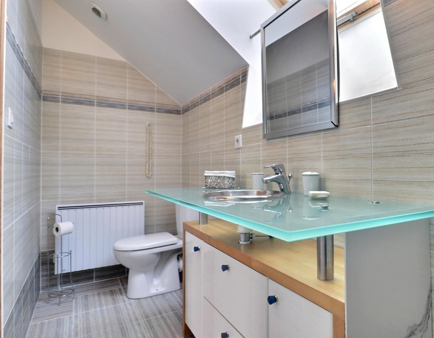 Et moderne badeværelse med vask i glas, hvid toilet og bruseområde.