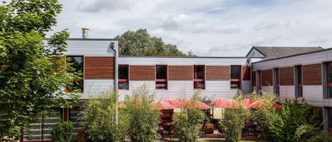 A modern building with a flat roof, large windows, and a covered outdoor seating area.
