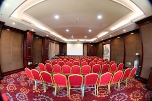 Una sala de conferencias con disposición circular de los asientos, una pantalla de proyector y suelo alfombrado.