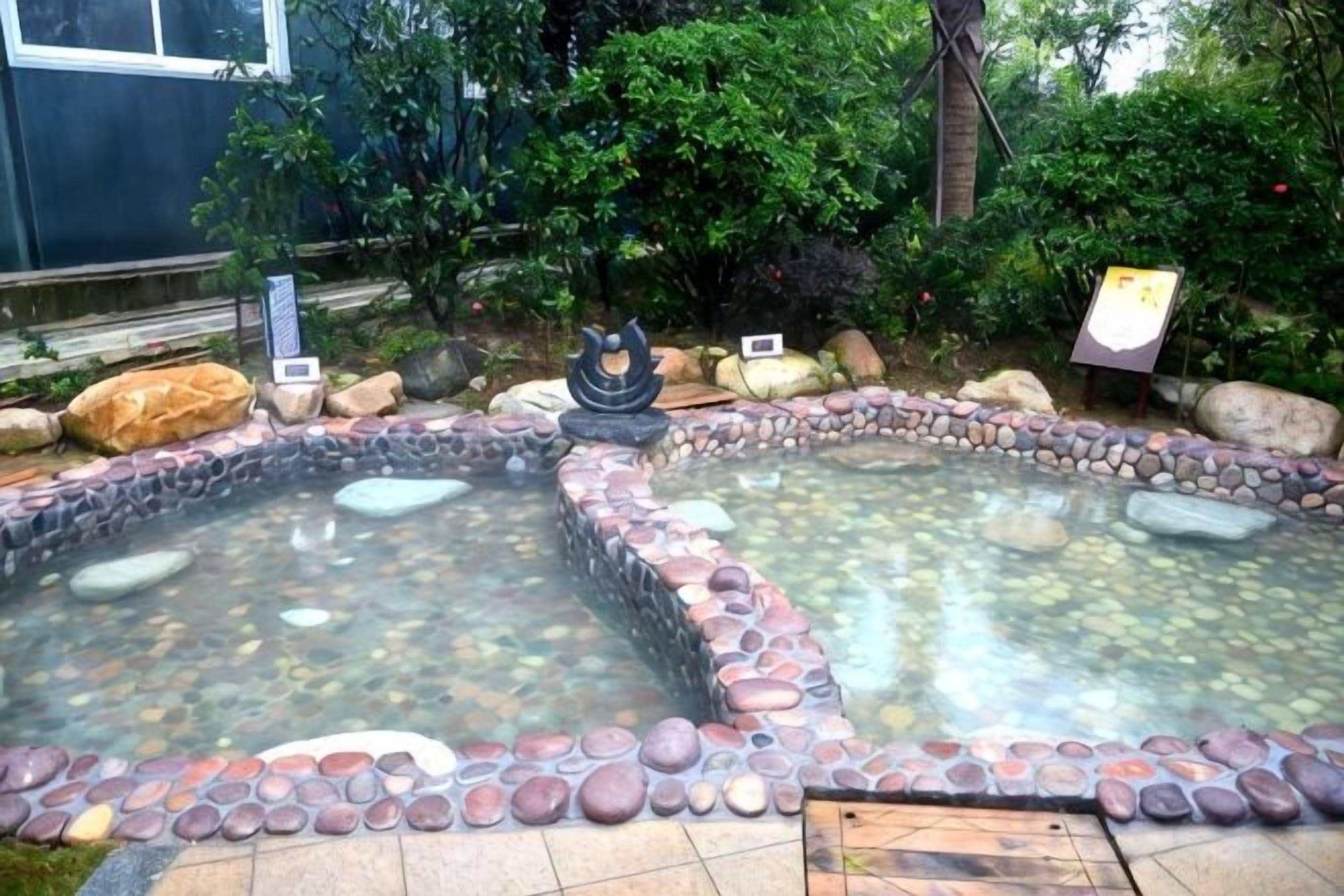 Un área de aguas termales con dos piscinas rodeadas de rocas y una pequeña estatua en el centro.