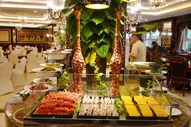 A buffet with various food items, a chandelier, and a large plant.