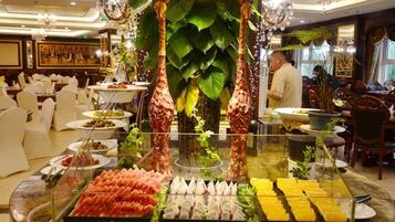 A buffet with various food items, a chandelier, and a large plant.