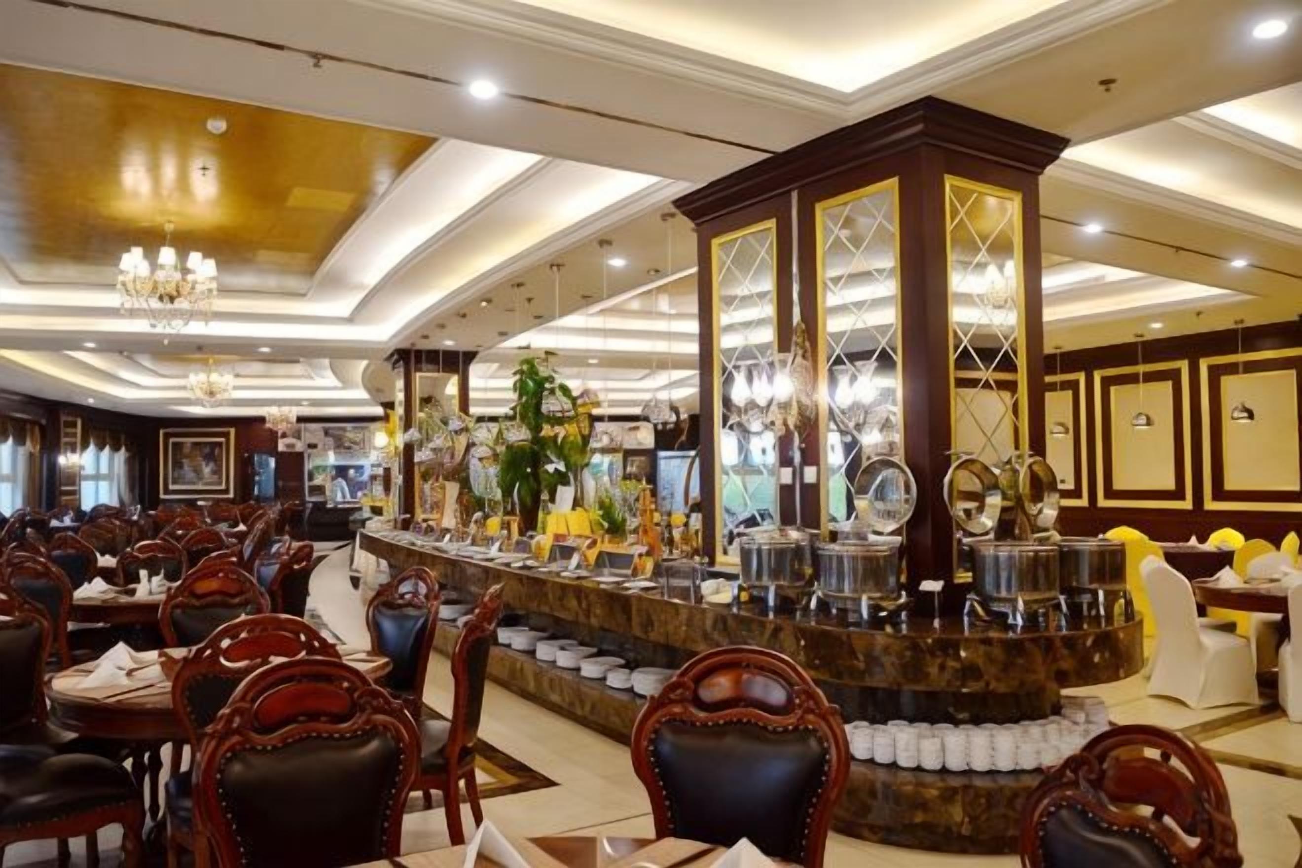 A spacious hotel lobby with a central bar area, multiple seating arrangements, and a chandelier.