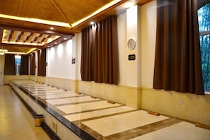 A hotel corridor with a long row of rooms, wooden ceiling beams, and a trash bin. - Aohua International Hot Spring Hotel (Linyi)