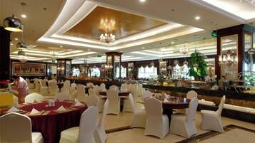 A banquet hall with round tables and white chairs, a bar area, and a chandelier.
