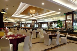 A banquet hall with round tables and white chairs, a bar area, and a chandelier. - Aohua International Hot Spring Hotel (Linyi)