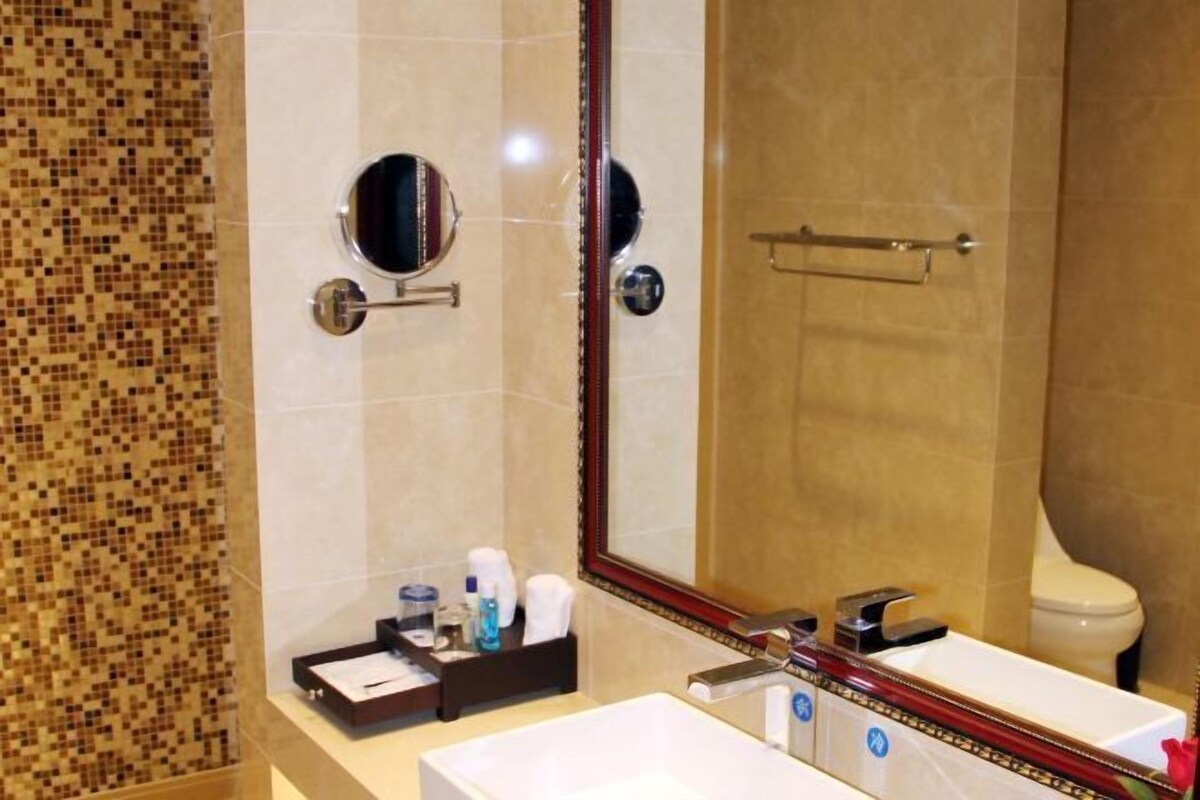 A bathroom with a tiled wall, a sink, a mirror, and a toilet.