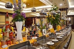 A buffet setup with multiple serving stations, a variety of food items, and decorative plants.