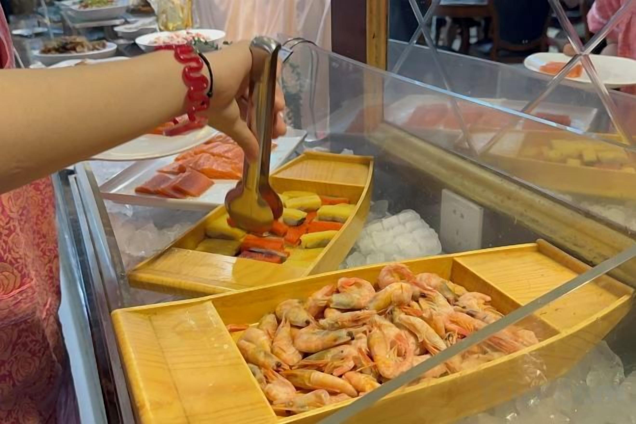 A person selecting food from a buffet with various dishes visible.
