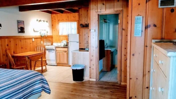 A cabin with a wooden interior, a dining area with a table and chairs, a kitchenette with a stove and refrigerator, and a bathroom with a shower. - 01-The Cascade Falls studio at the Washoe (South Lake Tahoe)