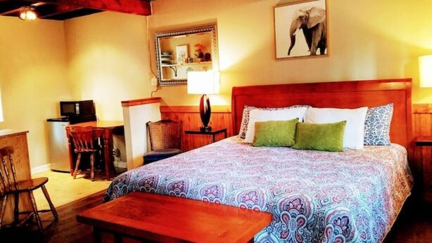 Ein Schlafzimmer mit einem großen Bett, einem hölzernen Kopfteil, einem Schreibtisch mit Stuhl, einem kleinen Tisch und einer Lampe.