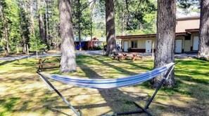 A hammock between trees, picnic tables, and a building with a red roof.