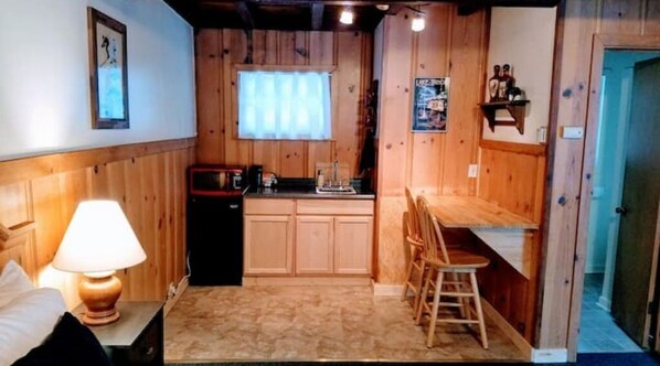 Une cuisine compacte avec des meubles de rangement en bois, un évier et un petit coin repas équipé d’une chaise.