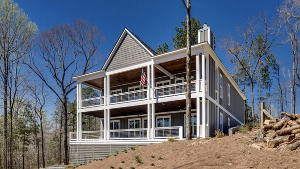 Une cabane à deux étages avec un balcon, entourée d’arbres et sous un ciel dégagé.