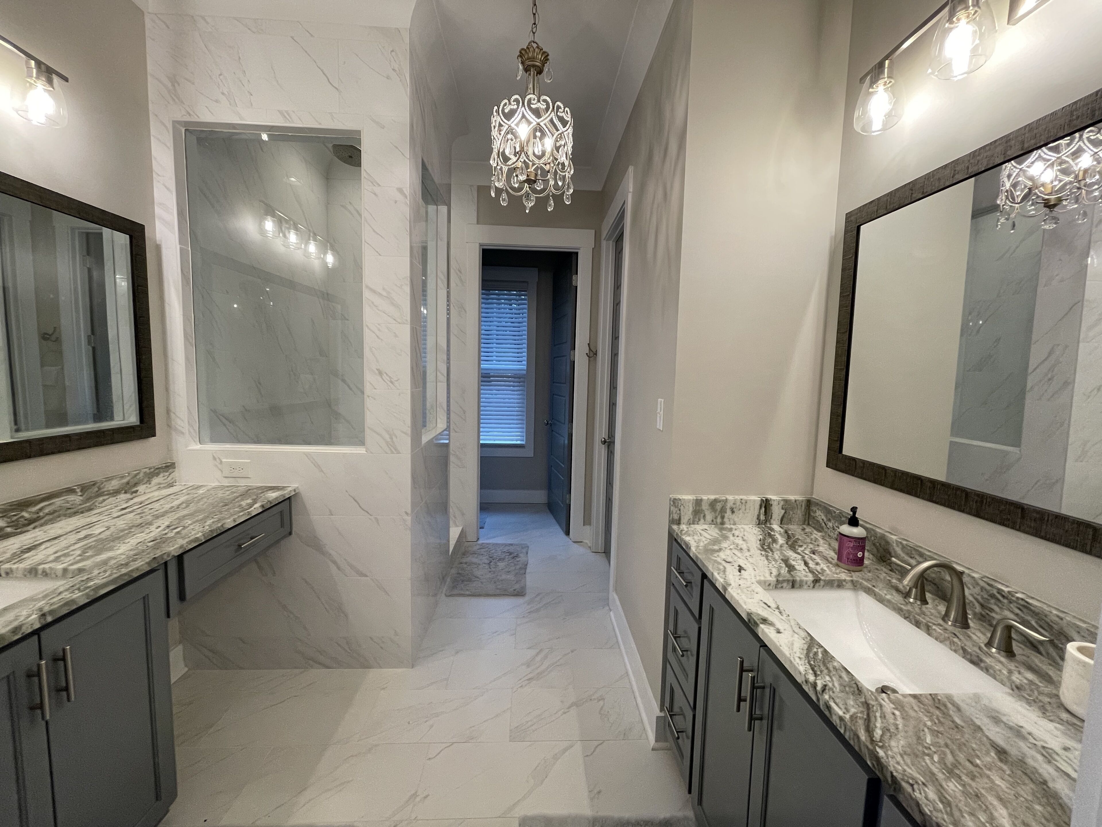Une salle de bain moderne avec un grand miroir, des plans de travail en marbre et un lustre.