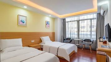 Quarto de hotel com duas camas, uma escrivaninha, uma cadeira, uma mesinha e uma janela com cortinas.