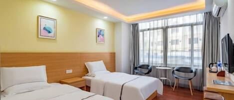 Ein Hotelzimmer mit zwei Betten, einem Schreibtisch, einem Stuhl, einem kleinen Tisch und einem Fenster mit Vorhängen.