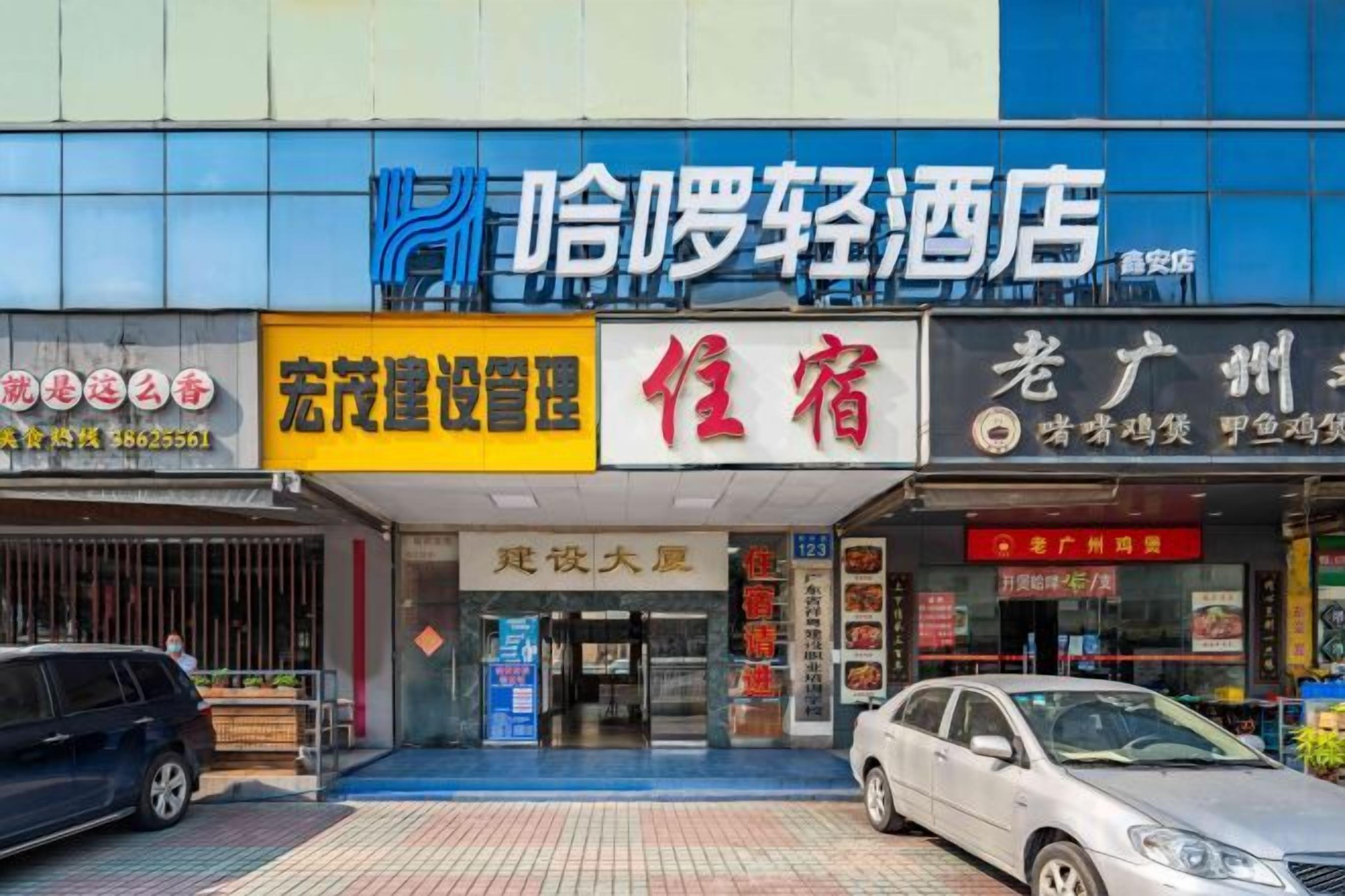 La façade d’un hôtel, avec une enseigne indiquant « 哈罗轻酒店 » et « 宏茂建设设计 ».