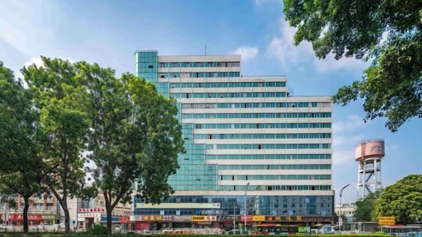 Ein modernes, mehrstöckiges Gebäude mit Glasfassade, umgeben von Bäumen und blauem Himmel.