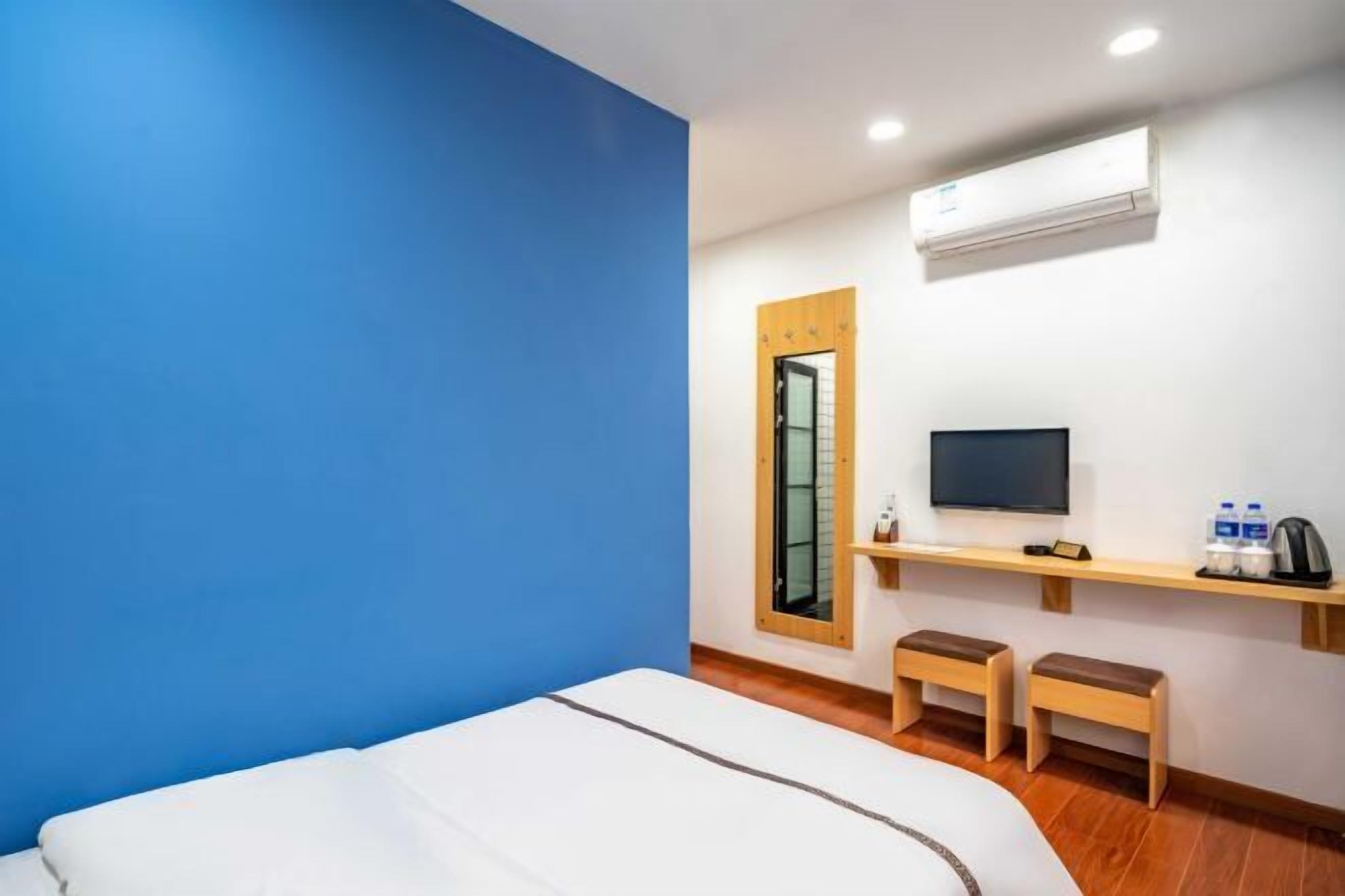 A hotel room with a bed, a TV, a shelf with toiletries, and a window with a wooden frame.