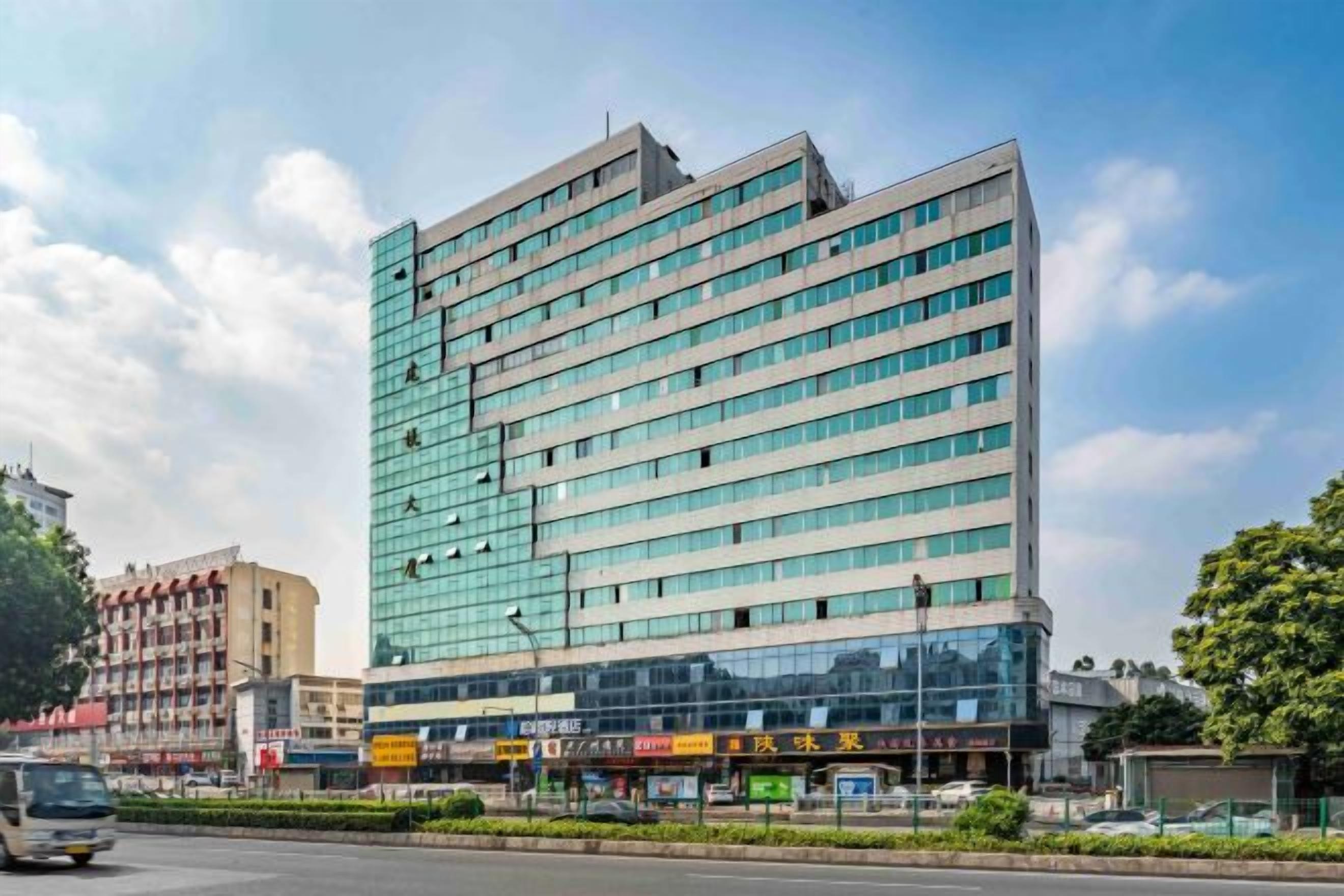 Un hotel de varios pisos con fachada moderna de vidrio, situado en una esquina con cielo despejado.