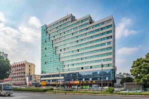 Un hôtel à plusieurs étages doté d’une façade moderne en verre, situé à l’angle d’une rue, avec un ciel dégagé.