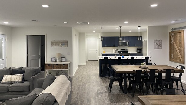 A modern living room with a grey sofa, a wooden dining table, and a kitchen in the background. - NEW! Countryside Retreat Home with Space for Entertaining, Weddings and More! (Minster)