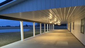 A covered outdoor area with a concrete floor, white columns, and a view of a body of water. - NEW! Countryside Retreat Home with Space for Entertaining, Weddings and More! (Minster)