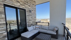 Ein moderner Balkon mit Ecksofa, Couchtisch und Glastür, welche auf eine Wüstenlandschaft hinausführt.