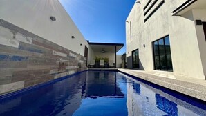 Ein moderner Swimmingpool mit einer klaren, blauen Wasseroberfläche, umgeben von einem weißen Gebäude mit großen Fenstern und einer gefliesten Wand.