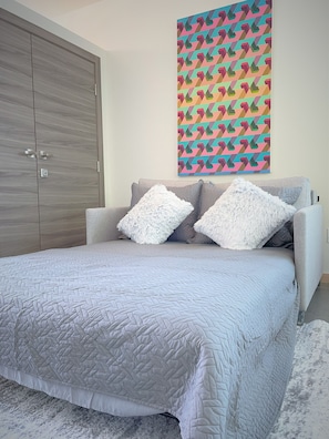 A bedroom with a bed, pillows, a wardrobe, and a colorful geometric wall art.