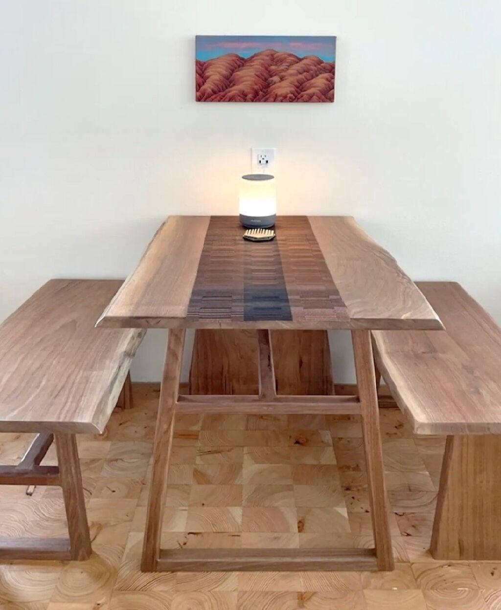 Une table de salle à manger en bois, avec une source de lumière centrale et un tableau accroché au-dessus.