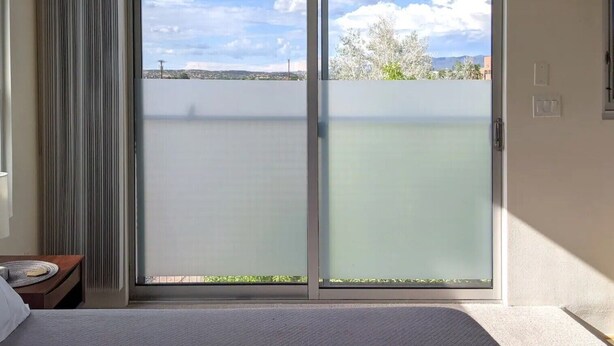 A room with a large sliding glass door leading to a balcony with a view of a body of water and distant hills. - The Tower - A Mountain View Escape (Santa Fe)