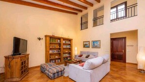 Ein Wohnzimmer mit einer Couch, einem Fernseher auf einer Holzkommode, einem Bücherregal und einem Fliesenboden.