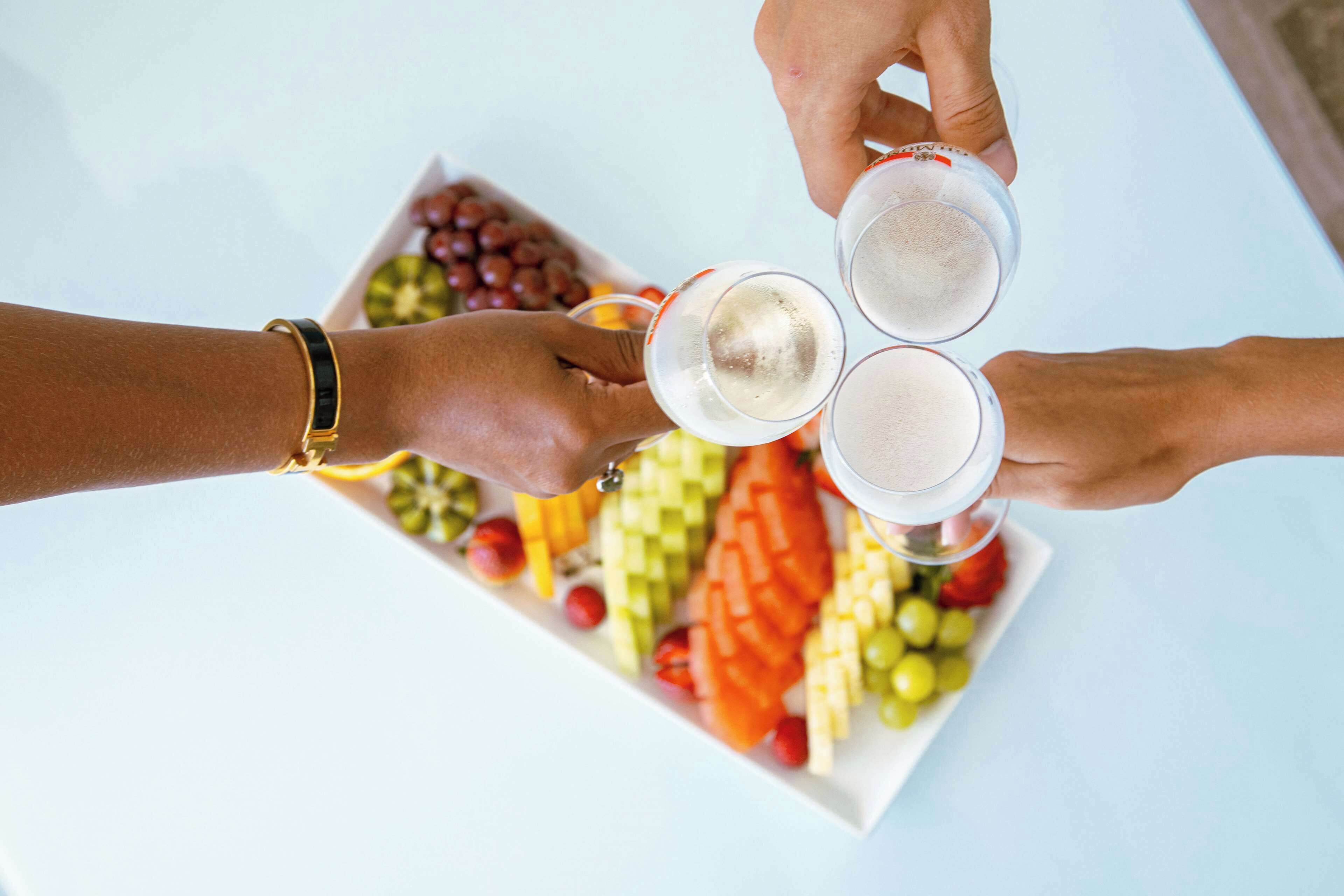 A group of people holding glasses of white beverage around a fruit platter.