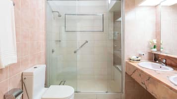 A bathroom with a glass-enclosed shower, a toilet, and a vanity with two sinks.