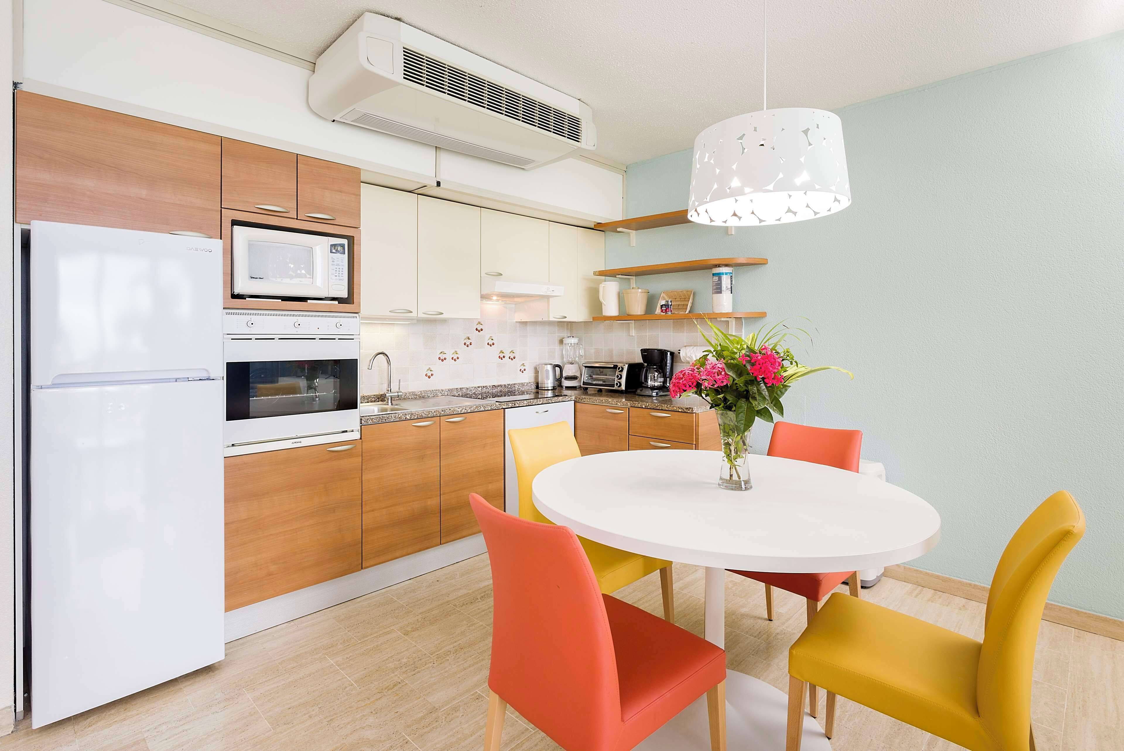 Una cocina moderna con microondas, horno y refrigerador. Hay una mesa de comedor con sillas y un florero con flores.