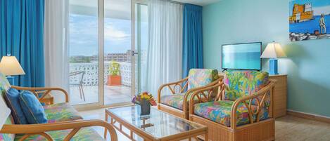 A room with wicker furniture, a glass coffee table, and a view of a cityscape through large windows.