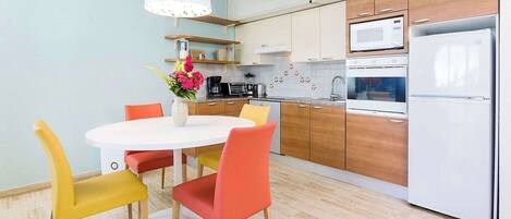 Una cucina moderna con mobili in legno, un frigorifero bianco e un'area pranzo con un tavolo rotondo e sedie colorate.