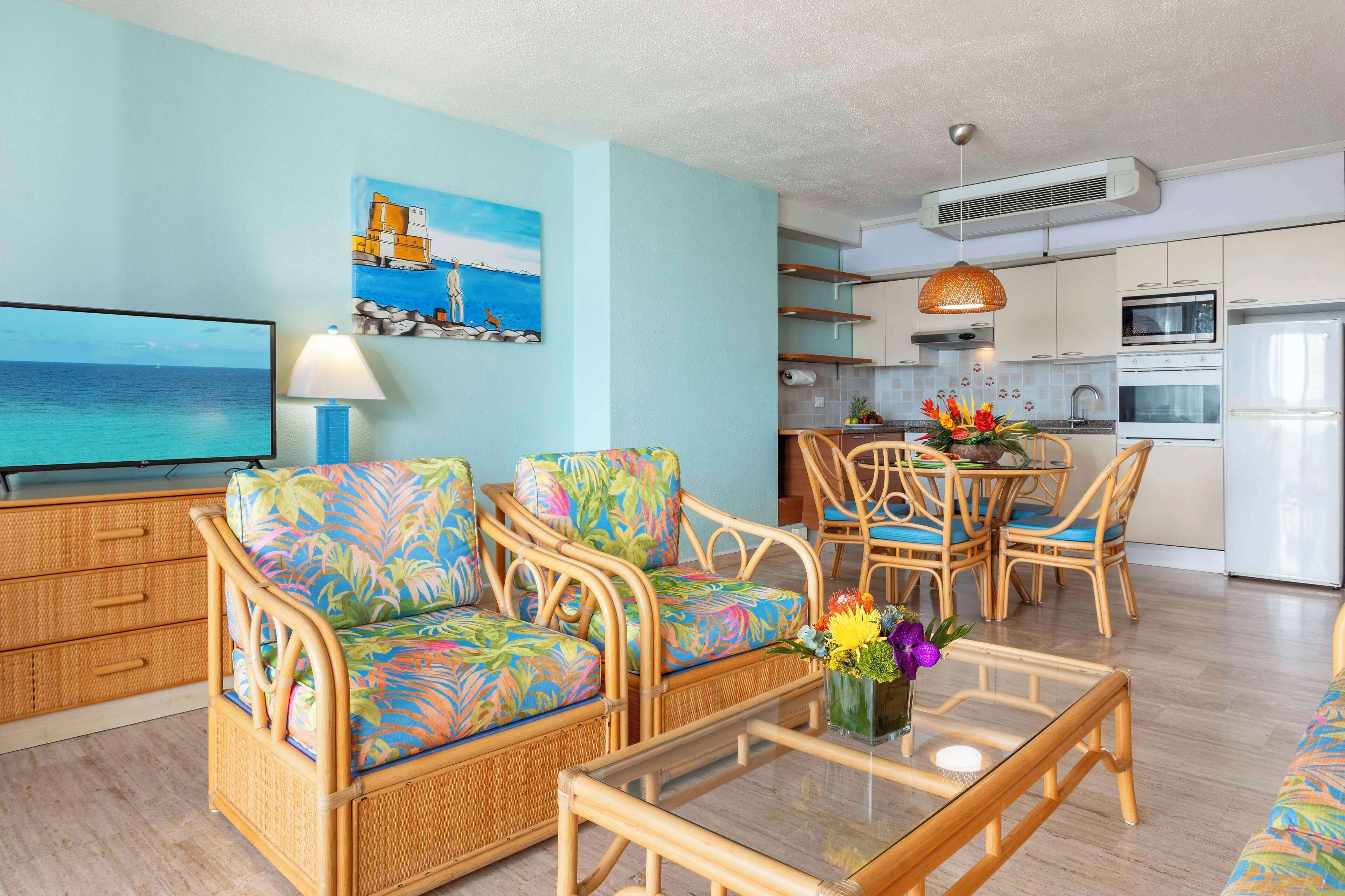 A living room with wicker furniture, a flat-screen TV, and a painting of a coastal scene.