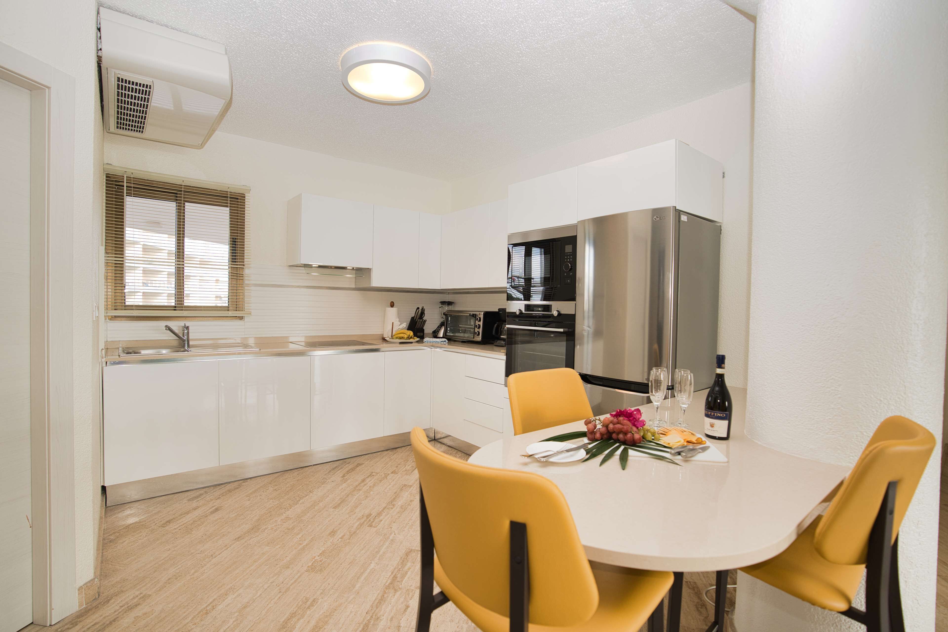 A modern kitchen with white cabinets, a stainless steel refrigerator, and a dining table with yellow chairs.